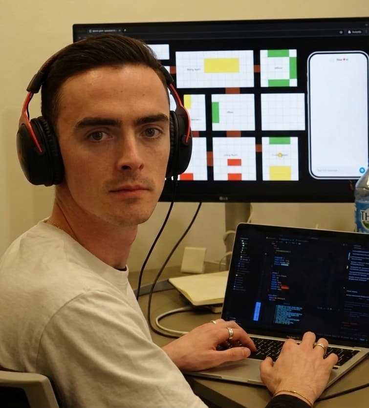 Remi at his desk, wearing headphones, with code on his laptop